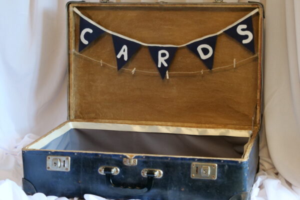 Vintage blue pasteboard suitcase, open, with blue bunting with the word 'Cards' in white.